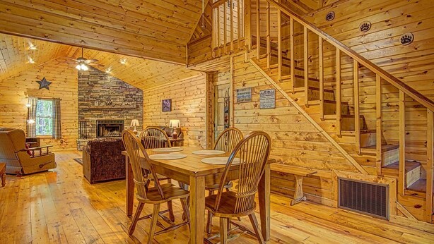 Interior de una cabaña de troncos con comedor, chimenea y escalera.
