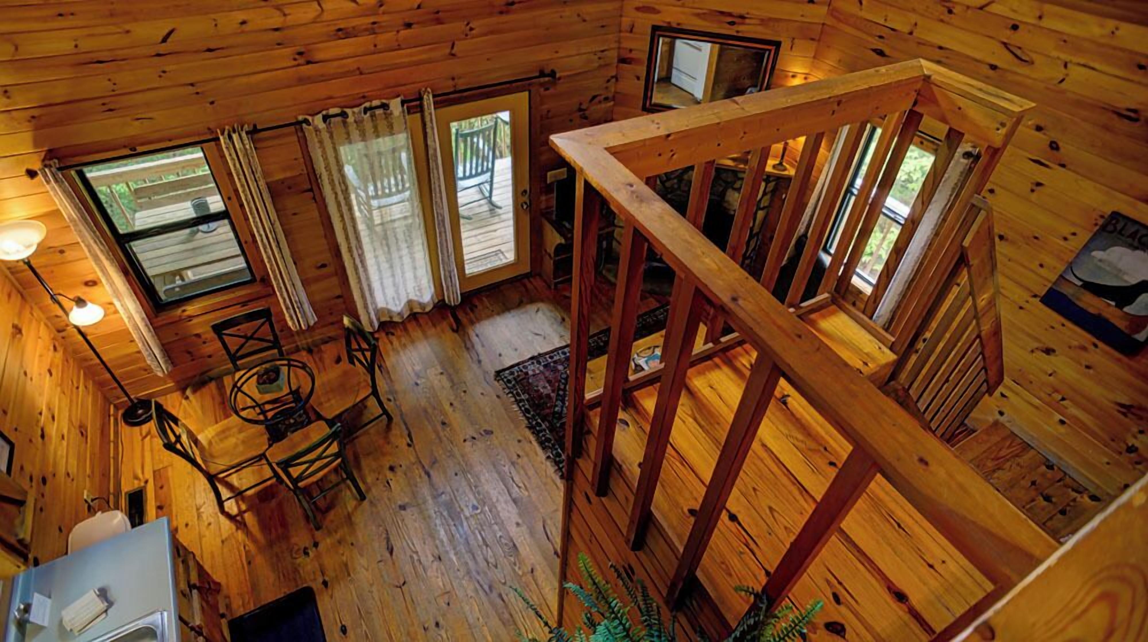 A cabin with wooden walls, a dining area with chairs and a table, and a staircase.