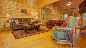 Un interior acogedor de cabaña de madera con piso de madera, dos sofás, una mesa de comedor y una zona de cocina.