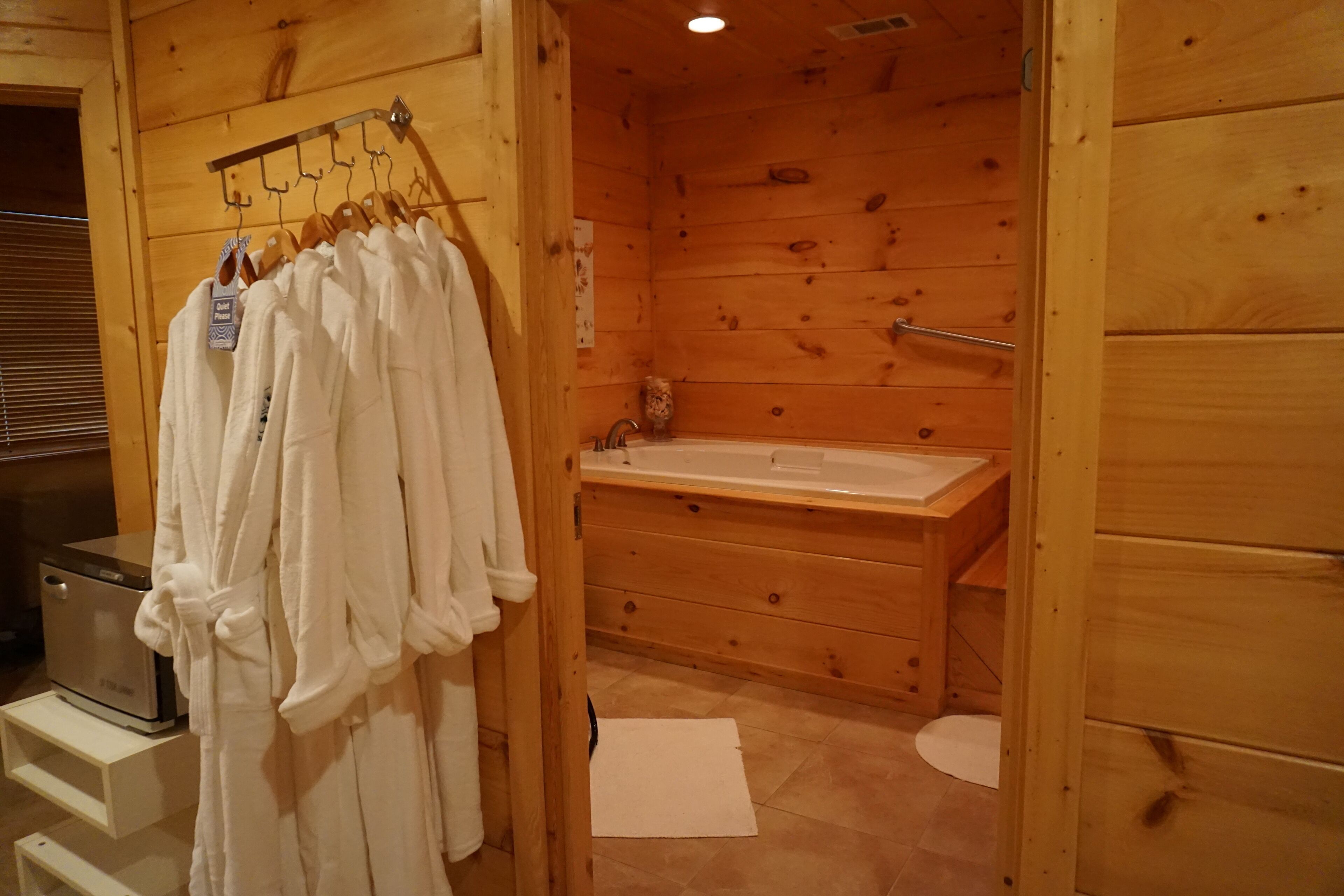 A wooden cabin bathroom with a wooden bathtub, a towel rack with white robes, and a small shelf with a heater.