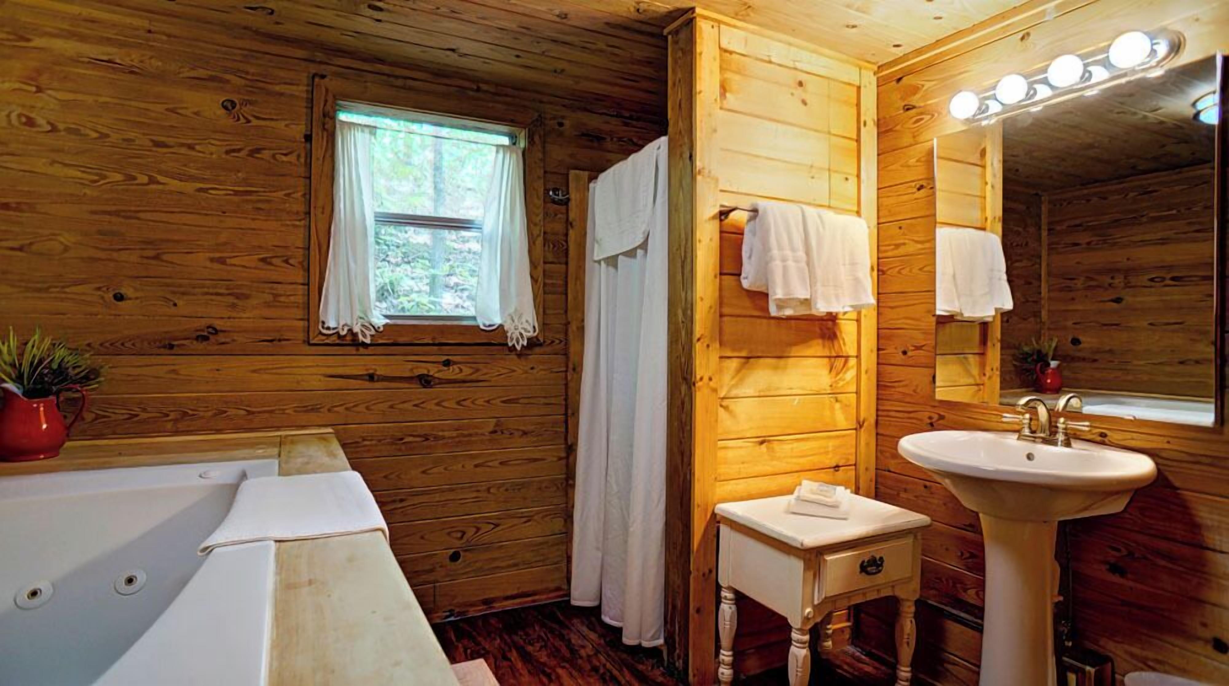 A wooden cabin bathroom with a bathtub, a sink, a mirror, and a window with curtains.