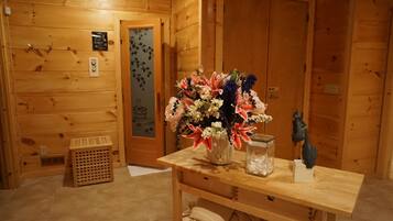A wooden interior with a wooden table holding a vase of flowers, a glass jar, and a small statue.