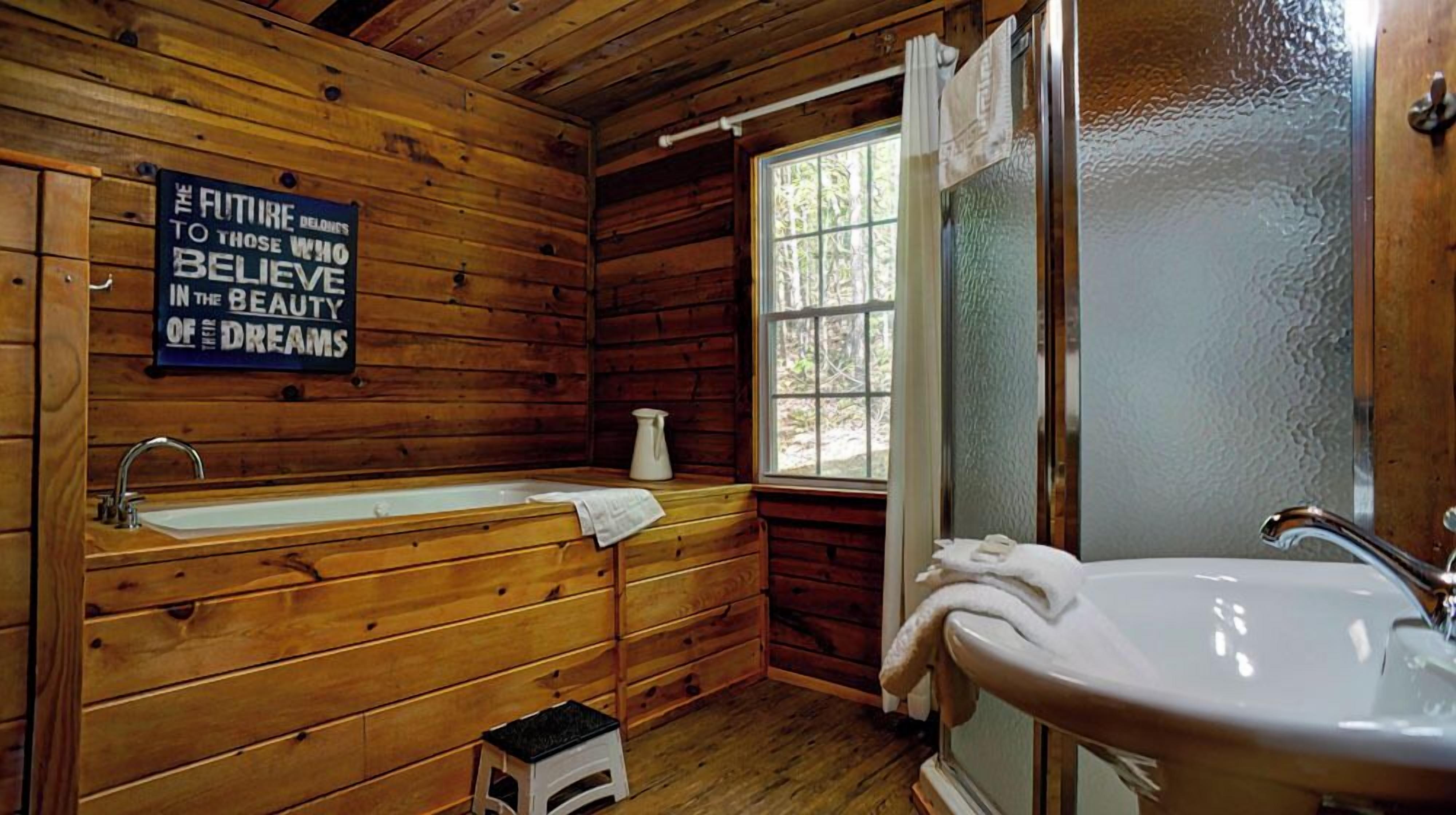 Baño de cabaña de madera con tocador de madera, lavamanos y bañera.