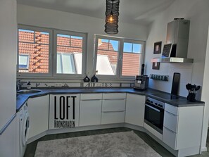 A modern kitchen with white cabinetry, a built-in oven, and a coffee machine. - Spacious loft in Kiel-Kronshagen (Kiel-Kronshagen)