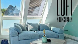 Un salon moderne avec un canapé d’angle, une table basse et une vue sur une maison grâce à des fenêtres de toit.