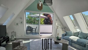 Un loft doté d’une grande porte-fenêtre coulissante, d’un coin salon confortable avec un canapé et des poufs, et d’une petite table.