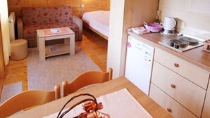 A cozy room with a wooden floor, a sofa, a bed, a small table, a chair, and a kitchenette with cabinets and a countertop.