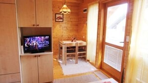 A cozy wooden cabin interior with a television, a dining table, and a window with curtains.