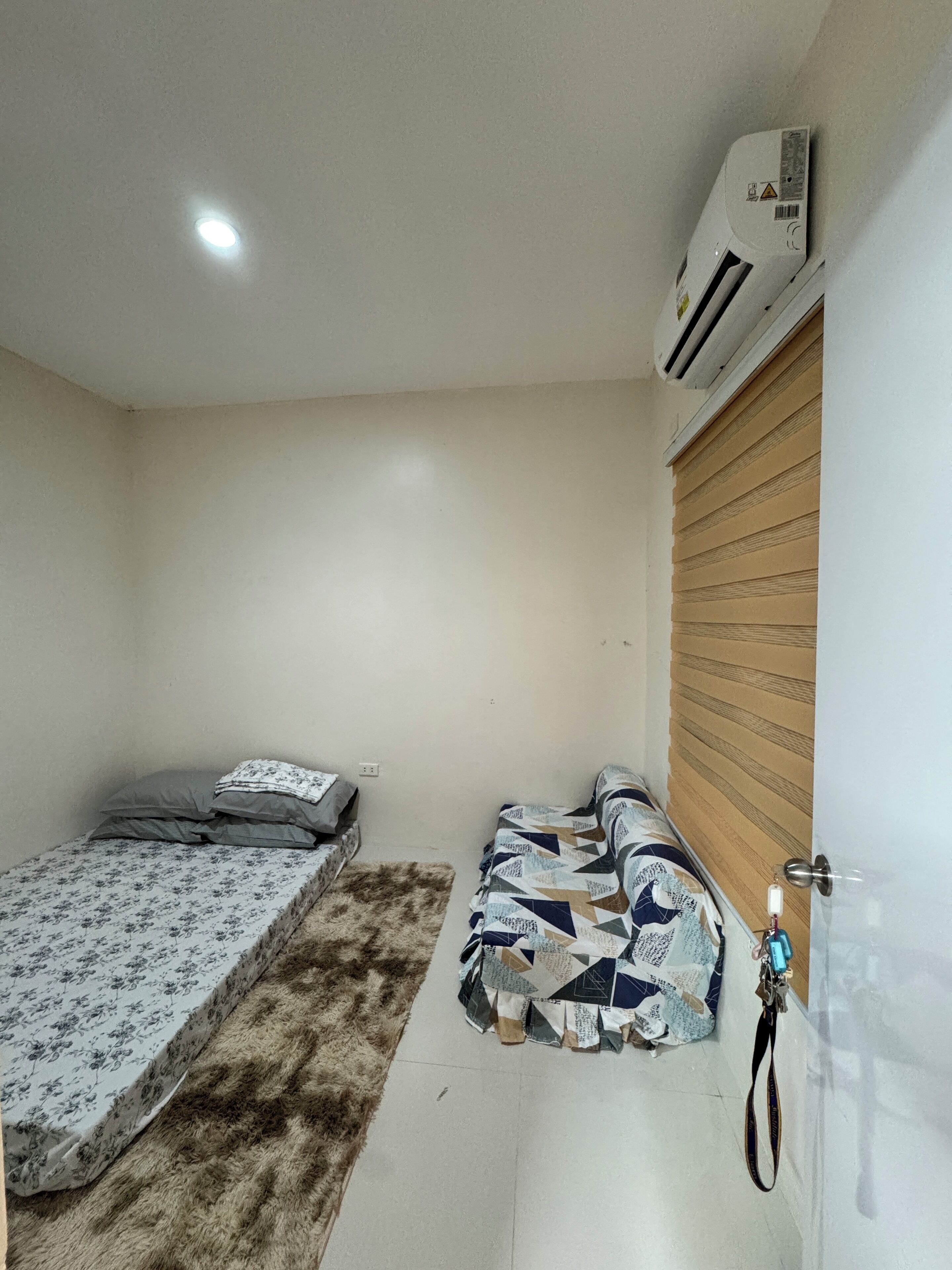 Een kleine, schone kamer met een enkel bed, een kleedje en een houten deur.