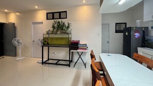 Een moderne keuken met een eettafel, stoelen, een koelkast, een waterdispenser, een ventilator en een klein aquarium.