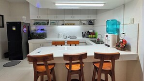 Een moderne keuken met witte kasten, een centraal eiland met barkrukken, een koelkast, een aquarium en een waterdispenser.