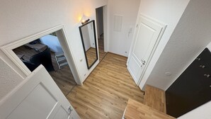 Ein Zimmer mit Holzboden, weißen Wänden und einer Tür zu einem weiteren Raum.