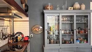 Une cuisine avec un plan de travail en bois, un meuble gris aux portes en verre et un sol carrelé.