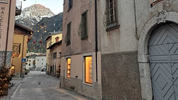 A narrow street with buildings on either side, featuring a mix of traditional architecture and a visible plaque on one building.