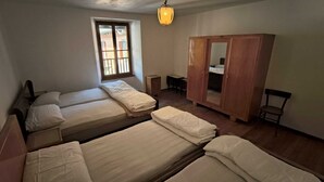 A room with two single beds, a wooden wardrobe, a small table, and a window with bars.