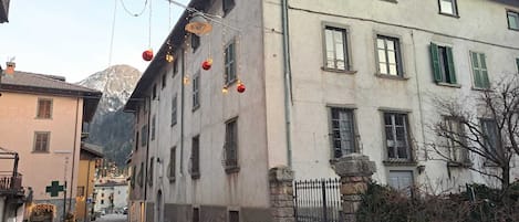 Una calle estrecha flanqueada por edificios, con una mezcla de estilos arquitectónicos, incluyendo un edificio de fachada de piedra y otro con exterior pintado.