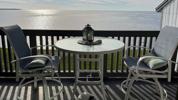 A round glass table with two chairs, a lantern, and a view of a body of water.