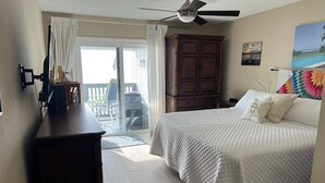A bedroom with a bed, a dresser, a ceiling fan, and a view of the outdoors.