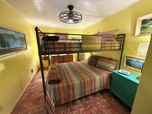 Ein Schlafraum mit Etagenbetten, einem Deckenventilator, einem Schreibtisch mit Lampe und einer Kommode.