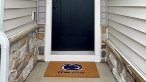 A black front door with a window, a stone wall foundation, and a doormat with the Penn State logo.