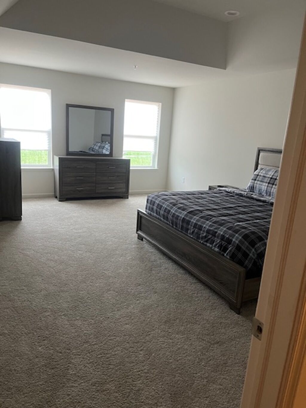 A bedroom with a large bed, a dresser, and a mirror. There are two windows providing natural light.