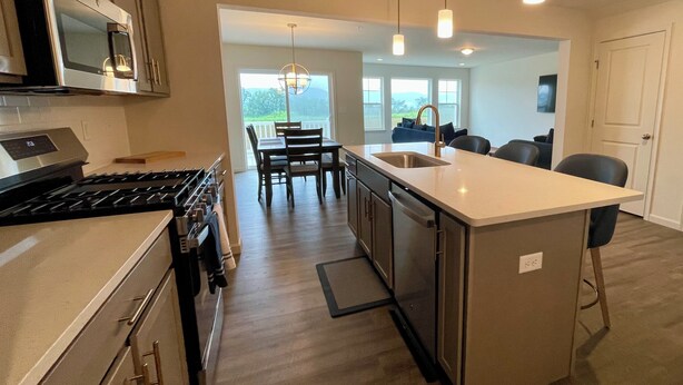 A modern kitchen with stainless steel appliances, a central island, pendant lighting, and a view to the outdoors.