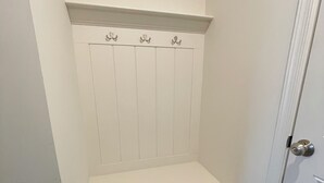 A white, narrow hallway with a door on the right and a small bench with hooks on the wall.