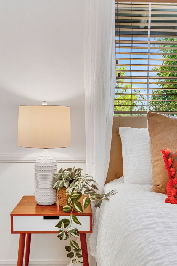 Un dormitorio con cama, una mesita de noche con lámpara y ventana con persianas.