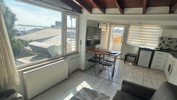 Ein modernes Wohnzimmer mit großem Fenster, einer Couch, einem Essbereich und einer Küche.