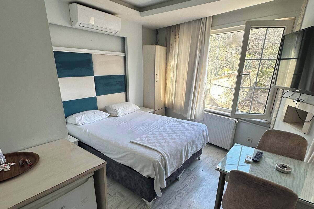 A modern hotel room with a bed, a small desk, a chair, and a window with curtains.