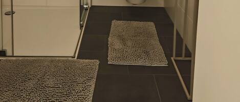 Un baño moderno con cabina de ducha de vidrio, azulejos blancos y suelo oscuro.