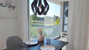 A dining area with a table set for two, a pendant light, and a view of a balcony with a railing and greenery.