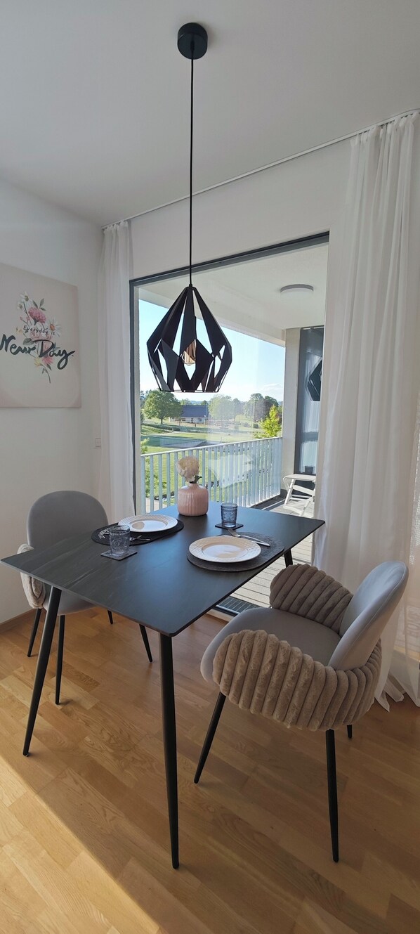 A dining area with a table set for two, a pendant light, and a view of a balcony with a railing and greenery. - Holiday Apartment "Seagull" (Salem)