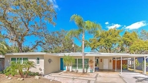 A single-story house with a covered porch, a front yard with a palm tree, and a clear blue sky.