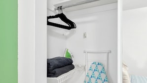 A bedroom with a bed, a hanging laundry rack, and an ironing board.