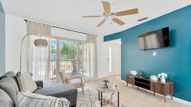 A modern living room with a sofa, a chair, a coffee table, and a TV mounted on a blue wall.