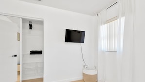 A bedroom with a bed, a TV mounted on the wall, a wardrobe, and a window with curtains.