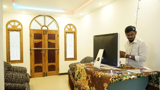 A room with a desk, a computer, and a person working. There are two doors with glass panels and a window. - Sobia Villa (Jaffna)