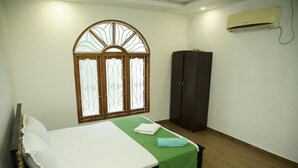 A bedroom with a bed, a wardrobe, a window with decorative glass, and an air conditioning unit. - Sobia Villa (Jaffna)