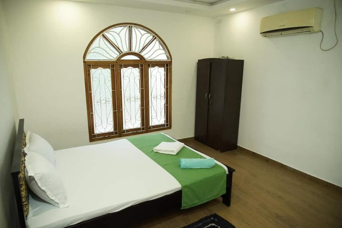 A bedroom with a bed, a wardrobe, a window with decorative glass, and an air conditioning unit.