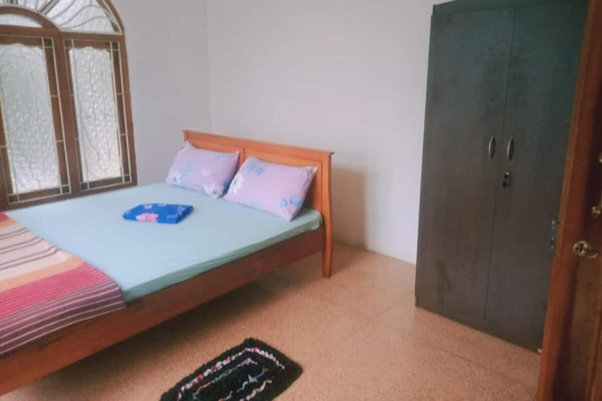 A bedroom with a bed, a wardrobe, and a window with a decorative grille.