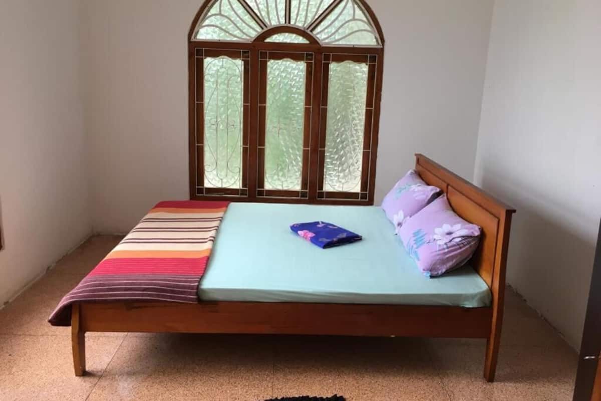A single bed with a wooden frame, a window with a decorative arch, and a striped blanket.