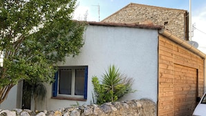 A rustic building with a stone wall, a wooden door, and a window with blue shutters.