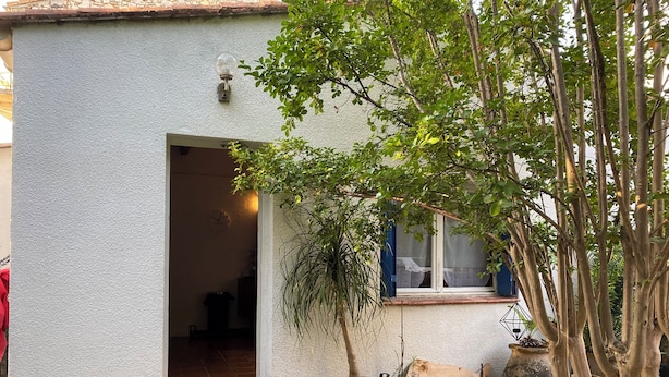A small, single-story building with a white exterior, a visible entrance, and a window with a curtain.