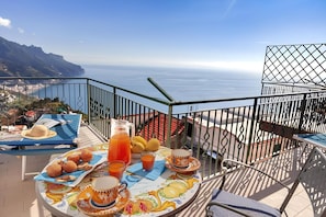 A balcony with a table set for breakfast, overlooking a coastal view.