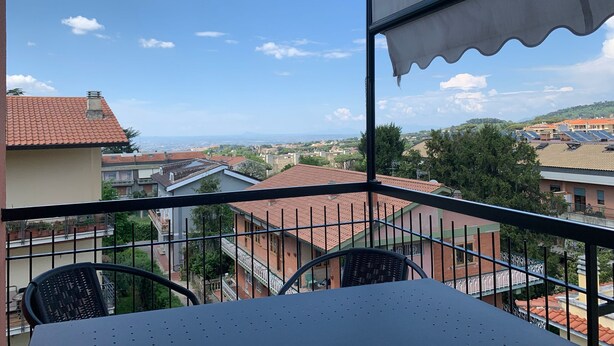 A balcony with a table and chairs, overlooking a residential area with red-tiled roofs and a clear blue sky. - Cozy apartment 2 steps from Rome finely renovated and equipped (Marino)