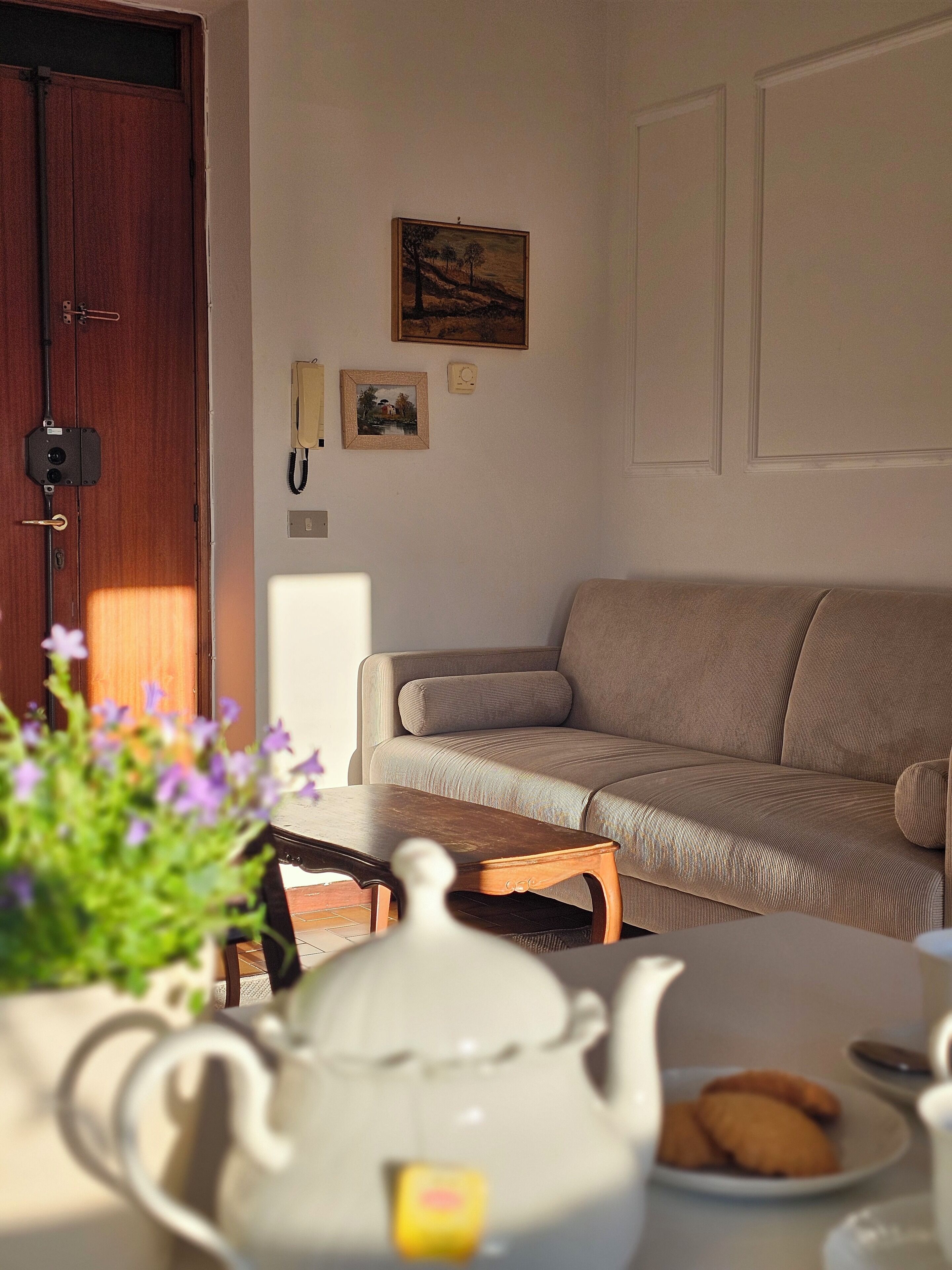A cozy living room with a sofa, a wooden coffee table, and a white teapot on a table.