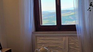 A bedroom with a bed, a window with a view of the countryside, a tea set on the bed, and a wall with a textured design. - Elegance and relaxation between Rome and Florence, in the heart of central Italy (Giove)