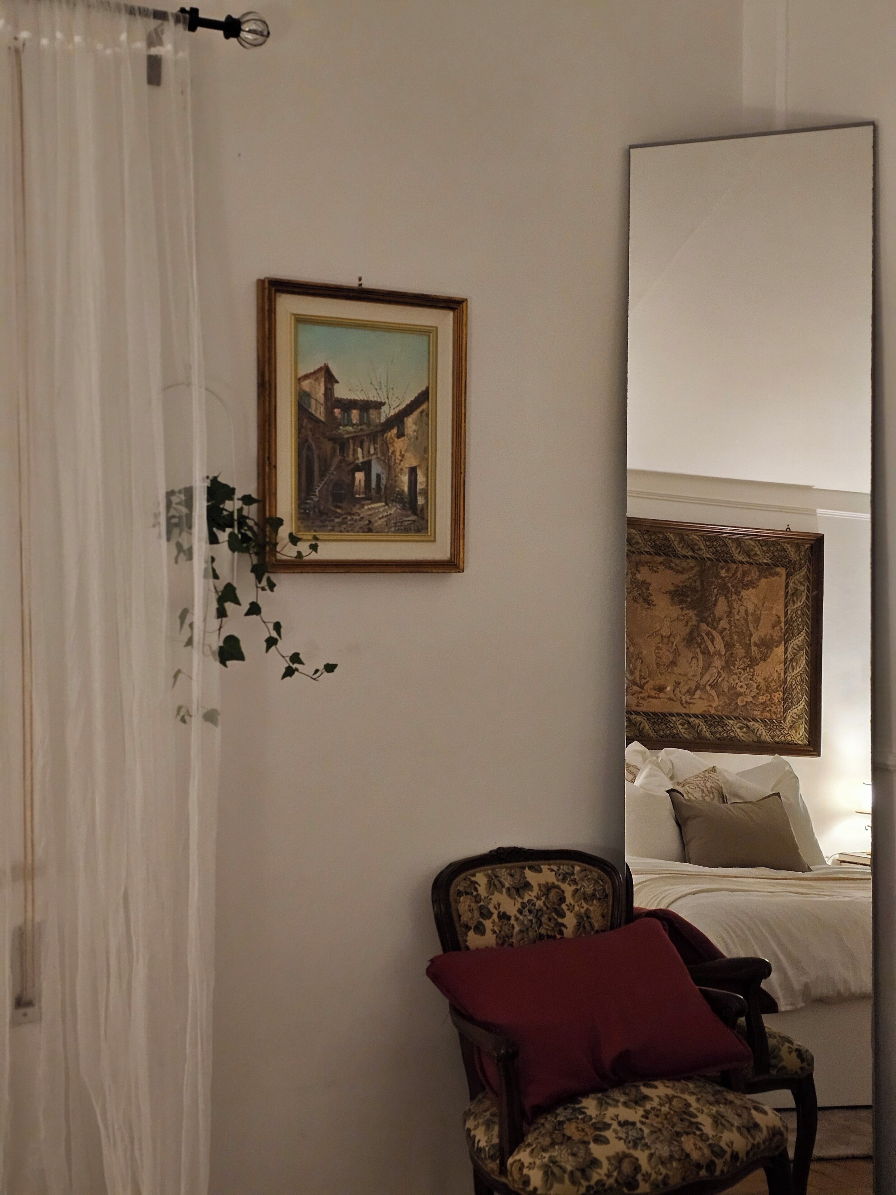 A bedroom with a bed, a chair, a painting, and a curtain.