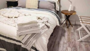 Un lit bien fait, recouvert d’une couverture à motifs, une table de chevet avec une lampe et un petit tabouret.